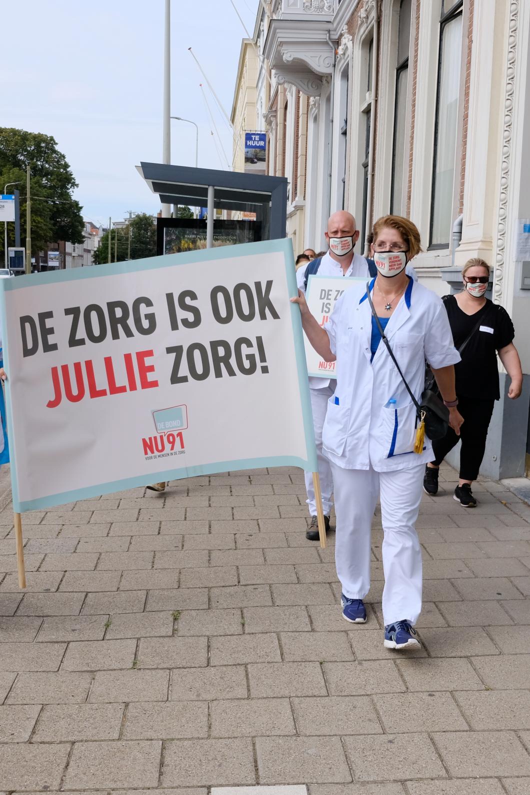 Twee vrouwen met witte kleding houden een poster vast met erop: De zorg is ook jullie zorg