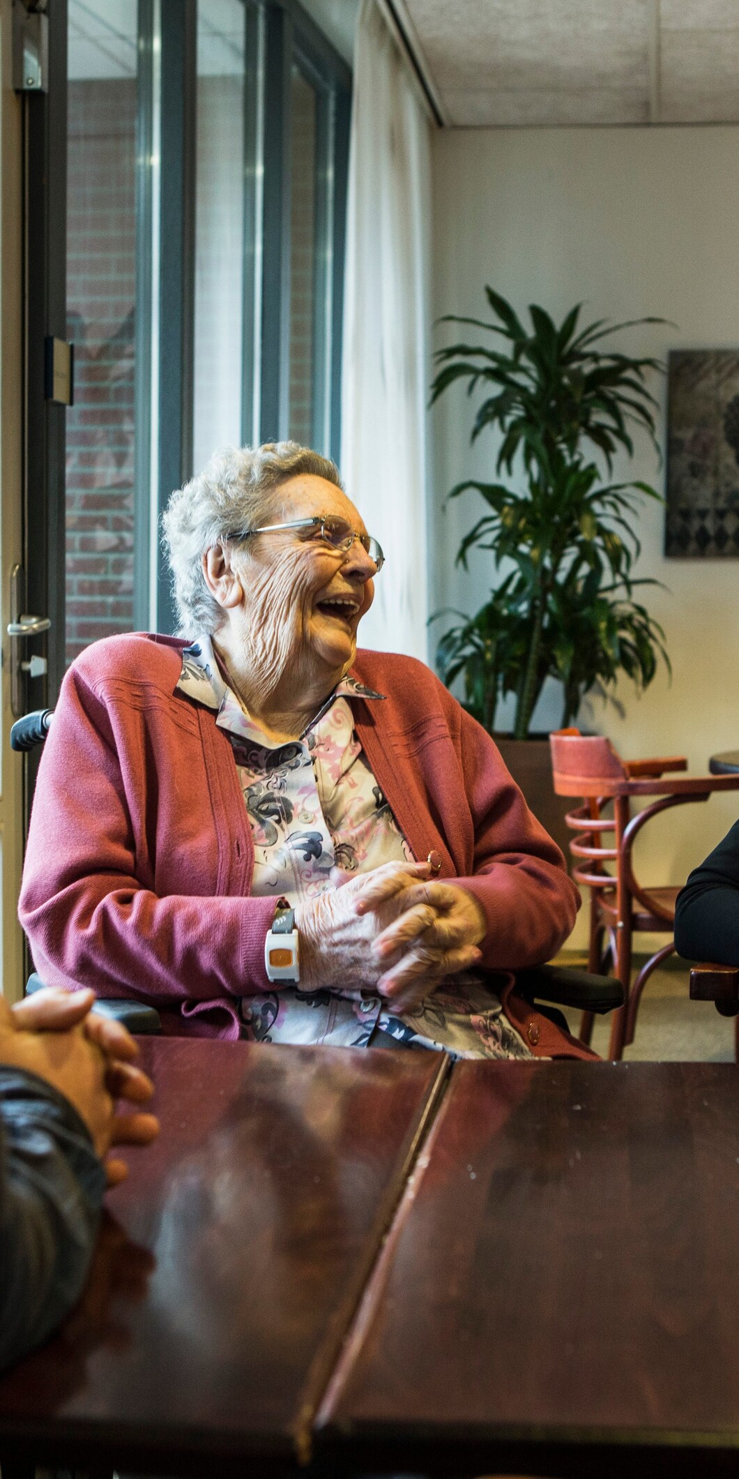 Een lachende oudere vrouw zit aan tafel met een jongere vrouw en een man