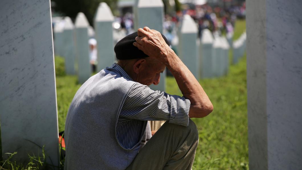 Een oude man zit op een begraafplaats in Srebrenica en houdt zijn hoofd vast