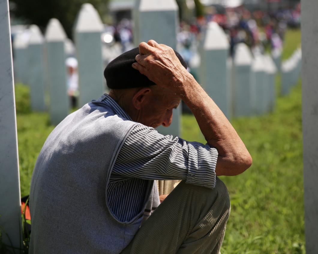 Een oude man zit op een begraafplaats in Srebrenica en houdt zijn hoofd vast