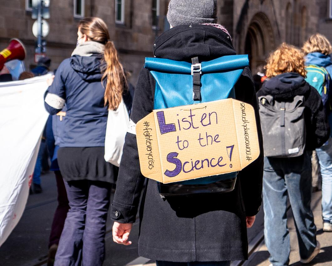 Beeld van een protestbord met daarop 'Listen to the science!'