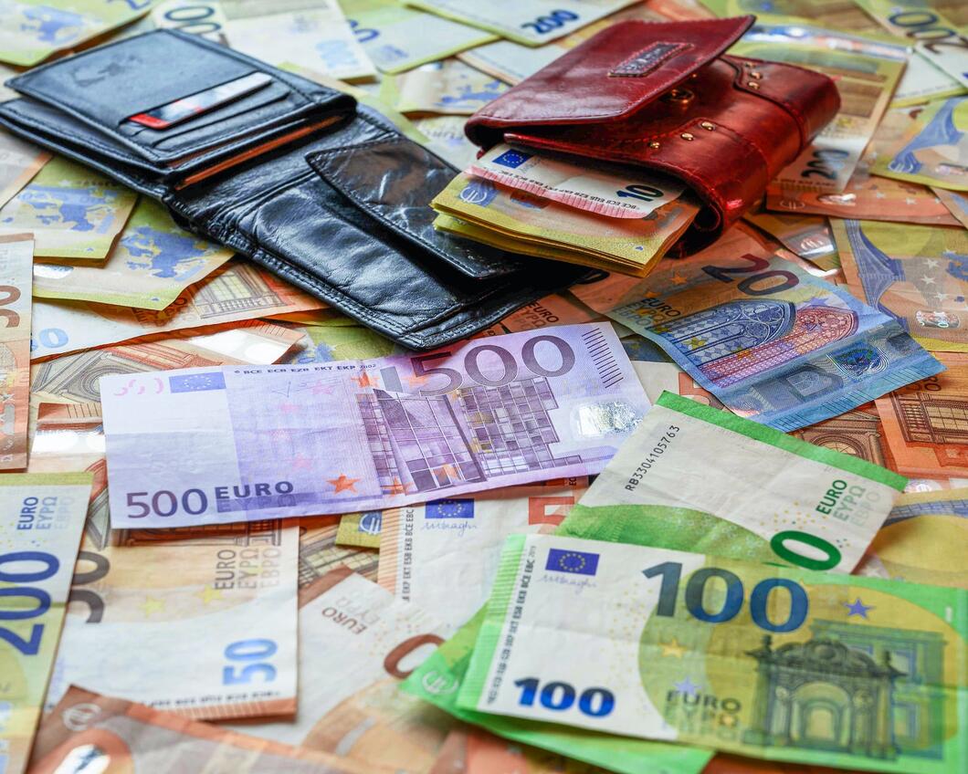 een tafel vol met eurobiljetten variërend van 20 tot 500 euro. Daar bovenop liggen twee portemonnees waar geldbiljetten uitpuilen.