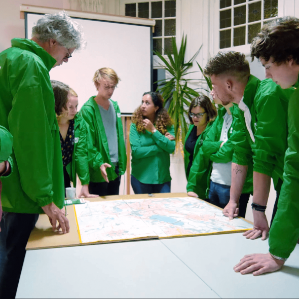 Een groep vrijwilligers in GroenLinks jasjes staan rond een tafel