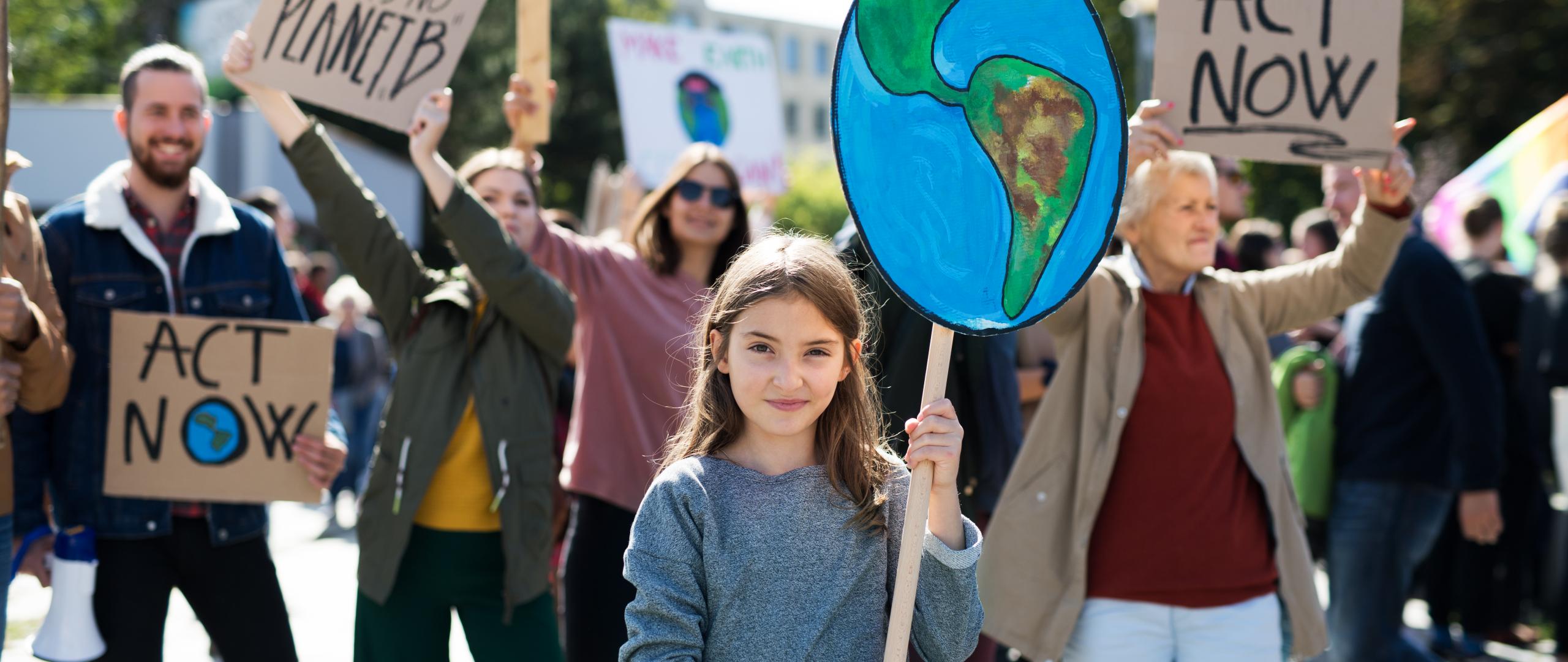 Een meisje met een bord van de aarde bij een groep mensen die actievoeren voor het klimaat