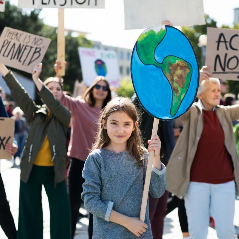 Een meisje met een bord van de aarde bij een groep mensen die actievoeren voor het klimaat