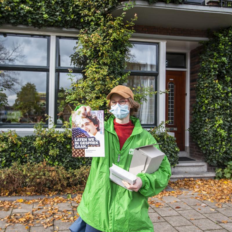 Een vrijwilliger in GroenLinks jasje houdt de brief van Jesse op. Ze draagt een mondkapje.