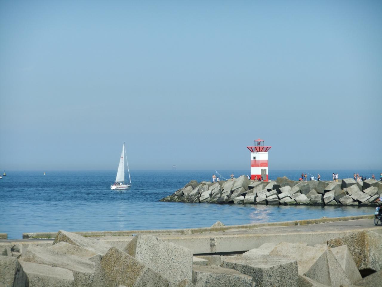 Een rood havenlicht op een pier van basaltsteen. Een zeilboot zeilt op zee.